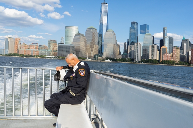 Bayonne, N.J. fireman on a ferry to New Jersey after the 9/11 Memorial Services, with lower Manhattan in background. Photo by Ben Sarao, on display in the 2023 NPC members photo exhibit.